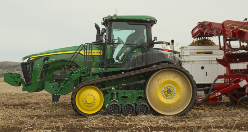 a farmer operating a tractor and harvesting implement loads a 10 wheeled seed potato truck.